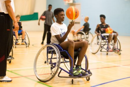 A young man in a wheelchair spins a basketball on an indoor court
