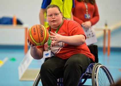 Female in a wheelchair passes a basketball on an indoor court