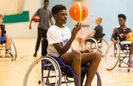 A young man in a wheelchair spins a basketball on an indoor court
