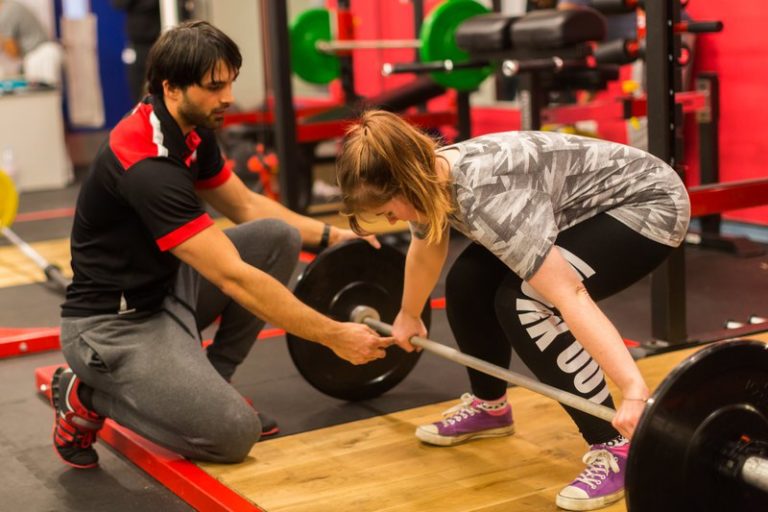 Young female during weights lifting session with the support of a supervisor