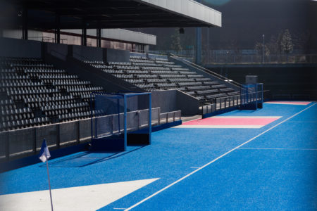 Empty stands facing a blue artificial hockey pitch