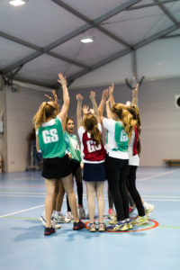 Two netball teams giving high-fives in centre of indoor court