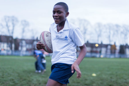Child carrying a rugby ball in a London park