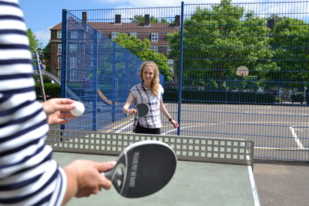 Two people playing table tennis at an outdoor table