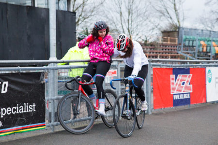 Two female cyclists resting at the side of an outdoor track