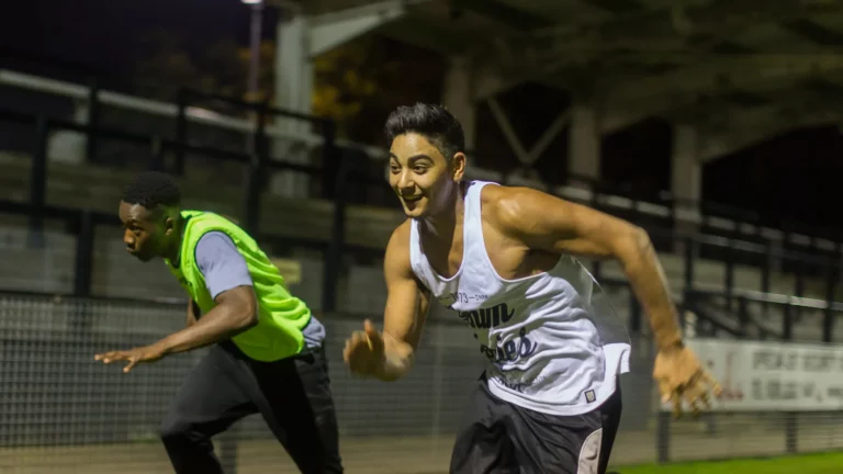 Two men running with railings and stadium seating behind.